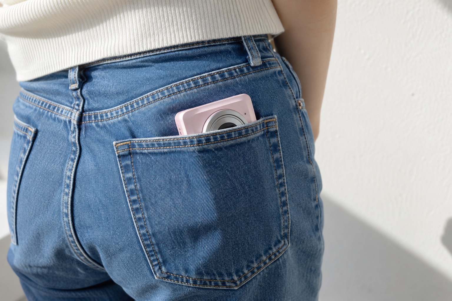 A pale pink compact digital camera peeking out of a jeans back pocket